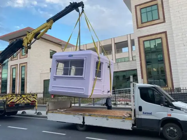 Truck-mounted crane lifting a lilac GRP kiosk off a delivery lorry on straps
